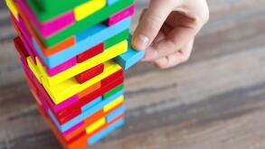 Close up of a hand pulling a colorful  jenga block from a big pile. Fun board games concept