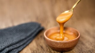 Manuka honey from New Zealand dripping from golden spoon in wooden bowl showing texture of natural healthy organic raw food.