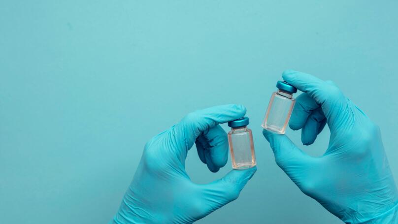 Doctor or nurse wearing blue surgical gloves holding a double vaccine dose