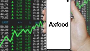 A man holds a smartphone displaying the logo of company Axfood listed on OMX Stockholm. Positive stock market background. Credit: PIXDUCE