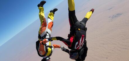 Skydiving team is holding hand together after they jumped out from a plane. Thereby they have fun and play in the blue sky.