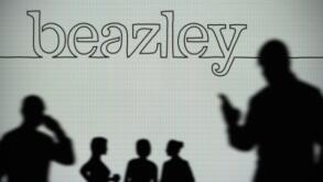 The Beazley Group logo is seen on an LED screen in the background while a silhouetted person uses a smartphone (Editorial use only)