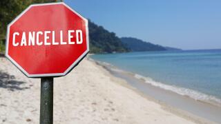 Red cancelled sign on beach background. COVID-19 pandemic quarantine. Cancelled vacation, travel, holiday plans because of corona virus.