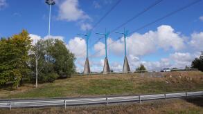 A scenic view of modern transmission towers on a green hill along the road on a sunny day