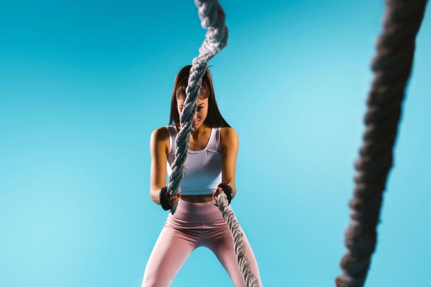 A strong, pumped-up girl in sport leggings throws a battle rope towards the camera. Blue background and empty side ad space.
