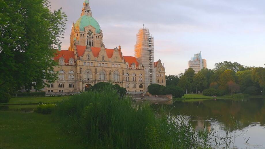 Rear view of Hannover City Hall with a reflective pond and surrounding park landscape.