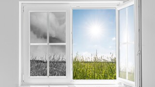 Half open window with view to the outside half on gray storm and half on clouds in blue sky with sun