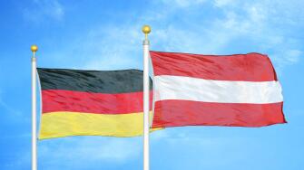 Germany and Austria two flags on flagpoles and blue cloudy sky