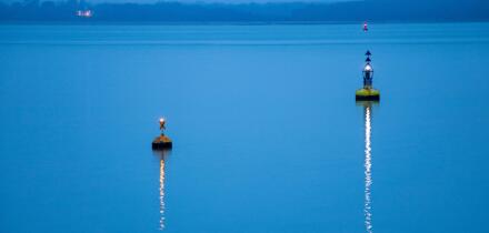 Two buoys marking the navigation channel.  Lights reflected on the water on a calm evening in winter.  The sea is pale blue.