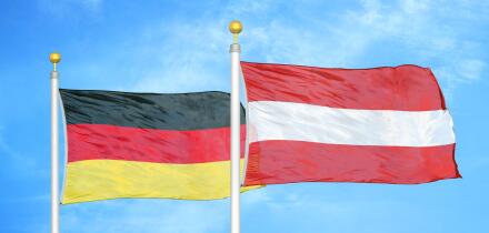 Germany and Austria two flags on flagpoles and blue cloudy sky