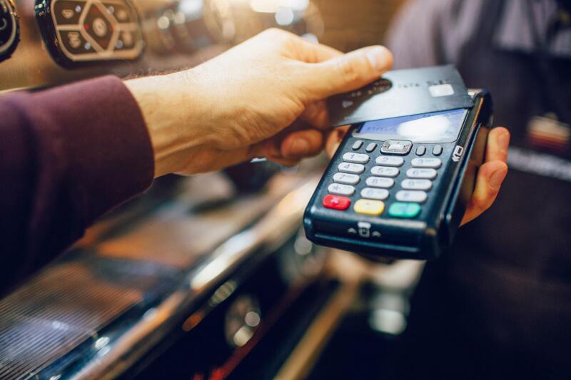 One hand hold machine for cards white another hold dark card for paying money. Men stand at coffee machine