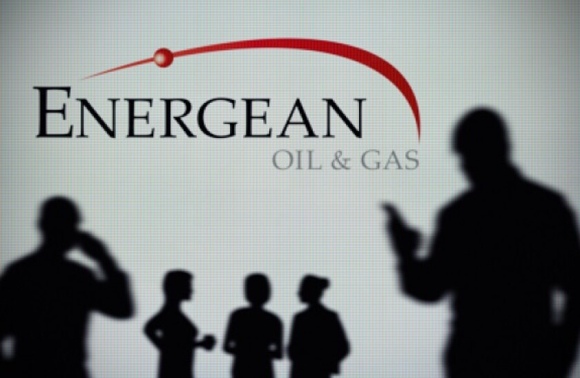 The Energean Oil & Gas logo is seen on an LED screen in the background while a silhouetted person uses a smartphone (Editorial use only)