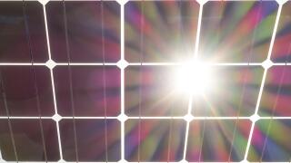 Solar panels wit sun burst flare. Solar panel seen from behind, underneath. Solar cells on clear glass with sun shining through.