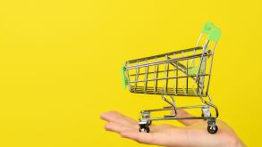 Empty shopping cart on female hand. Shopping theme. Small Trolley isolated on a bright yellow background. Consumer concept, Copy space.