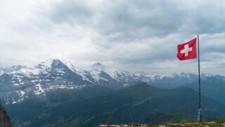 Swiss flag flown in strong wind. Bad weather, dark clouds, rain. In the background Eiger, Monch, and Jungfrau mountains.