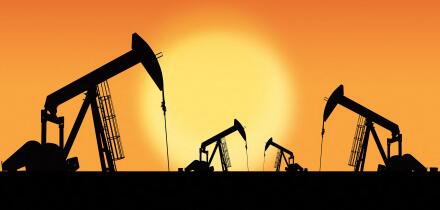 Rows of oil pumpjacks silhouette against a sunset sky with copy space. Oil and gas energy exploration.
