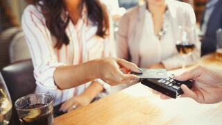 Woman paying bartender with credit card contactless payment at bar