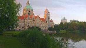 Rear view of Hannover City Hall with a reflective pond and surrounding park landscape.