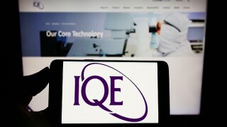 Person holding smartphone with logo of British semiconductor company IQE plc on screen in front of website. Focus on phone display.
