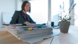Busy businesswoman doing paperwork in office at the desk filled with papers and documentation