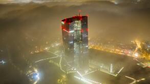 Aerial view of the European Central Bank skyscraper piercing through a sea of fog, its red lights ablaze against the muted city lights, Frankfurt am M