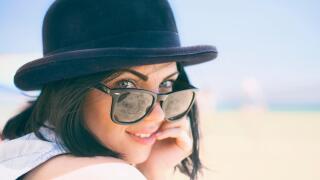 Portrait of smiling beautiful young woman in black hat. Model shooting on the beach.
