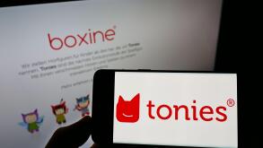 Person holding smartphone with logo of German audio toys company Boxine GmbH (Tonies) on screen in front of website. Focus on phone display.