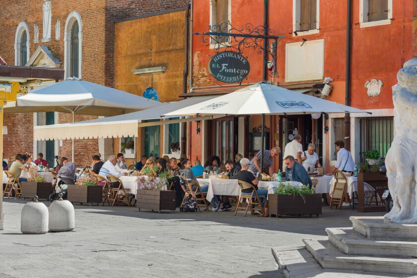 Restaurant piazza Italy, view in summer of a group of people dining outside a pizzeria in the scenic port of Chioggia, Comune of Venice, Italy
