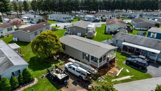 Gordonville, Pennsylvania, USA, April 30, 2024 - Aerial view shows mobile, manufactured homes lined along a tranquil street, surrounded by well-maintained lawns and trees. The sun casts a warm light, highlighting the neat layout and construction.