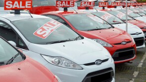 Sale of used Ford cars on car dealership pavement forecourt outside showroom arranged alternate red and white obscured number plates Essex England UK