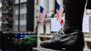 New York City, USA - June 20, 2018: Close up of foot  of George Washington statue in Federal Hall against New York Stock Exchange building in Wall Str