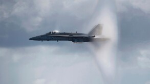 A US Navy F/A-18C Hornet breaks the sound barrier while flying over the aircraft carrier USS Carl Vinson.