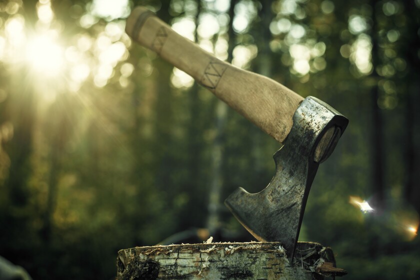 A woodcutter's big axe is stuck into a log in the forest, the setting sun in the background.Beautiful artistic photo of an axe.