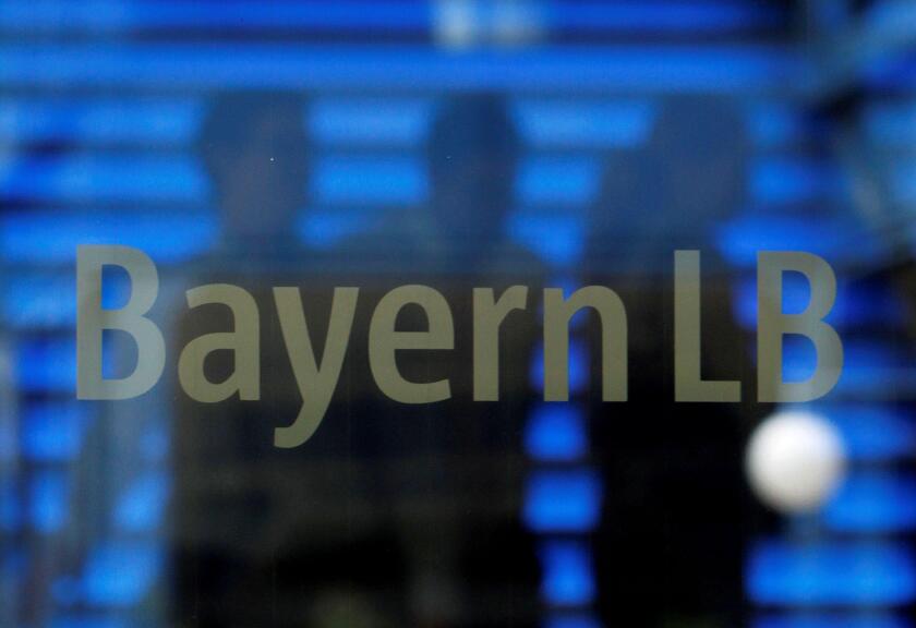 Employees of the Bavarian public sector bank BayernLB are silhouetted as they walk near the bank's logo at the BayernLB headquarters in Munich July 2, 2012.   REUTERS/Michaela Rehle/File Photo