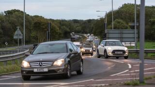 Cars with lights on in traffic being driven to work in the early morning rush hour, on the A27 road in the UK.