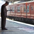 An elderly man reading a newspaper while waiting for a train.
