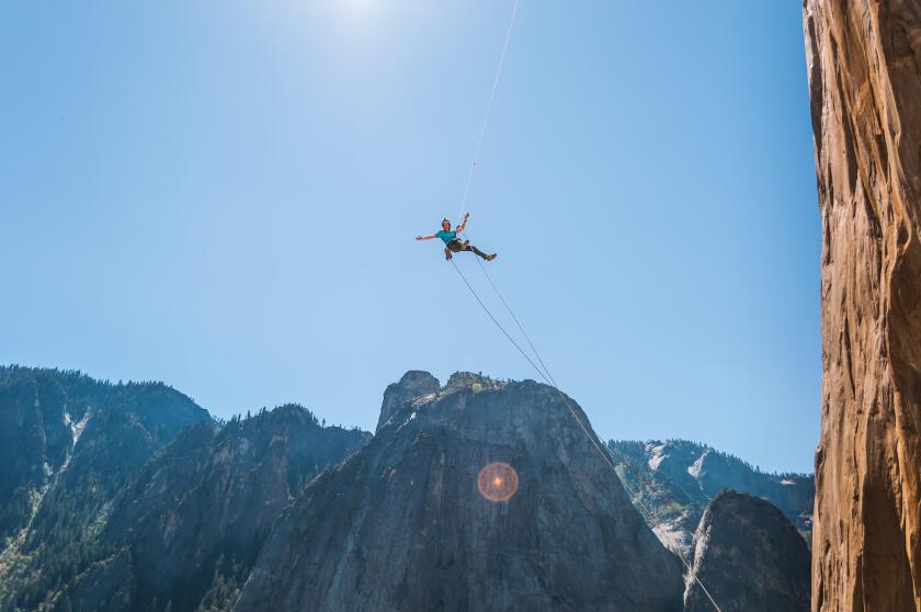 Person swinging mid air against blue sky on alcove swing at the base of El Capitan, Yosemite Valley, California, USA