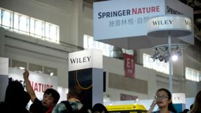 In this Aug. 23, 2017, photo, visitors browse vendor exhibits near a display from publisher Springer Nature at the Beijing International Book Fair in Beijing. Academic publisher Springer Nature said Wednesday, Nov. 1, 2017, that it has blocked access to a