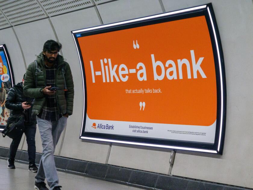 Commuters walk past an Advert for Allica Bank on wall of London railway station  London UK