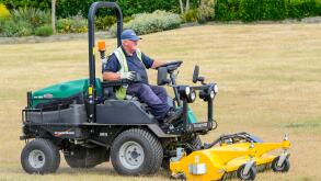 Old man riding on a Ransomes ride-on lawnmower while mowing and mulching the grass in a park.