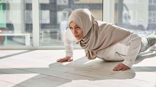 Determined Arab Muslim woman doing push-ups against the background of large windows at home on a beautiful sunny day. Home workout concept