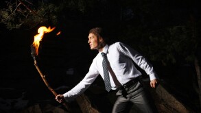 Image of brave man with burning stick in darkness