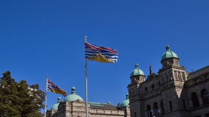 Two flags of the province of British Columbia fly in front of the legislature in Victoria.