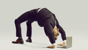 Happy flexible businessman in suit doing yoga while working on his laptop computer
