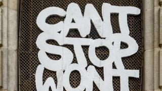 Graffiti with the message 'Can't Stop Won't Stop' on a wire mesh window grille in a historic stone doorway in Barcelona, Spain.