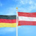 Germany and Austria two flags on flagpoles and blue cloudy sky