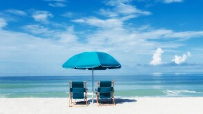 Two turquoise beach chairs under umbrella facing the ocean sea shore under sunny warm blue sky blue-green ocean
