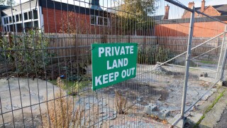 Derelict building plot surrounded by metal wire fencing and 'keep out' notice.
