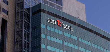 The contemporary glass and concrete facade of the ASN Bank building in Utrecht, with its distinct logo, stands prominently against a clear blue sky.
