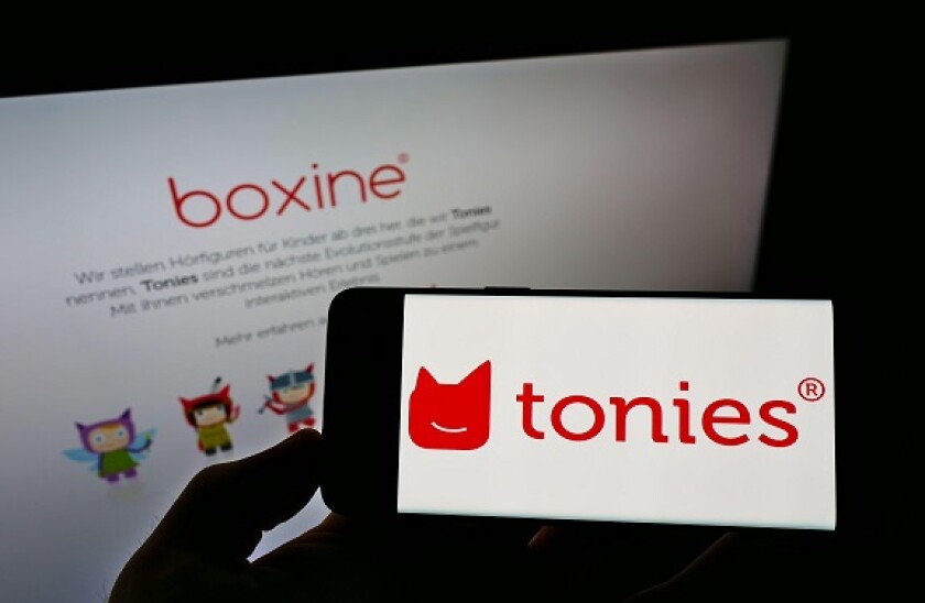 Person holding smartphone with logo of German audio toys company Boxine GmbH (Tonies) on screen in front of website. Focus on phone display.